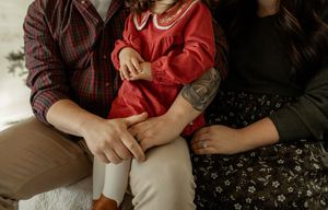 A person wearing a red sweater holds a small white kitten in their lap while sitting on a floral patterned couch.