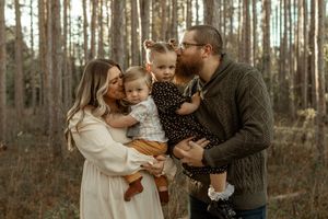 A loving family of three shares tender moments while walking among tall pine trees in a forest setting.