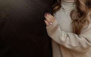 A person in a cozy beige turtleneck sweater poses against a neutral background with long wavy hair.