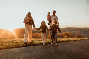 A group of people walking along a rural road at sunset, creating silhouettes against the warm golden sky.