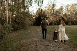 Couple walking hand in hand through a serene wooded area during golden hour.