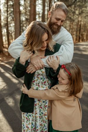 A family shares tender moments of laughter and embraces on a sunlit forest path.
