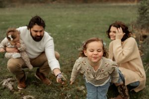 A loving family spends time together in a cozy outdoor photoshoot wearing neutral tones against a grassy backdrop.