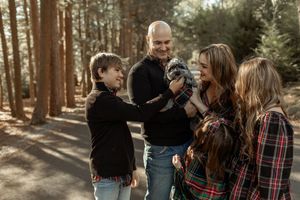 Family enjoying a playful moment together in a sunlit forest while wearing casual fall clothing.