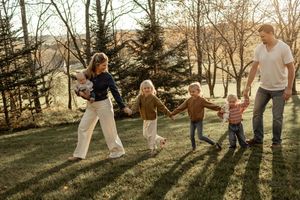 Silhouettes of a family playing and dancing together in a sunny park during golden hour with trees in background.