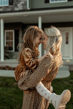 Two people in warm sweaters embrace and dance together on a grassy lawn in front of a house at dusk.