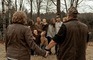 A group of people participate in a team building exercise outdoors in a wooded area during autumn.