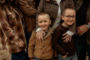 Two children wearing brown and burgundy sweaters smile together during an autumn family photo session.