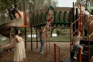 Family enjoying playful moments together at a rustic playground with natural lighting and trees in background.