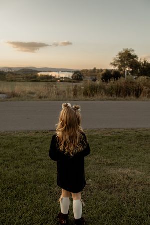 A person in black sits on grassy field during golden hour sunset with mountains and trees in the distance.