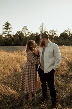 A couple shares an intimate moment in a golden field at sunset, with tall grass and trees in the background.