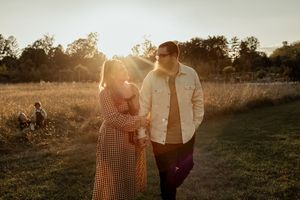 A couple shares a tender moment in a golden sunlit field during sunset while wearing casual attire.