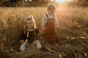 Children playing in a golden wheat field at sunset with sunlight creating a warm backlit glow through the grass.