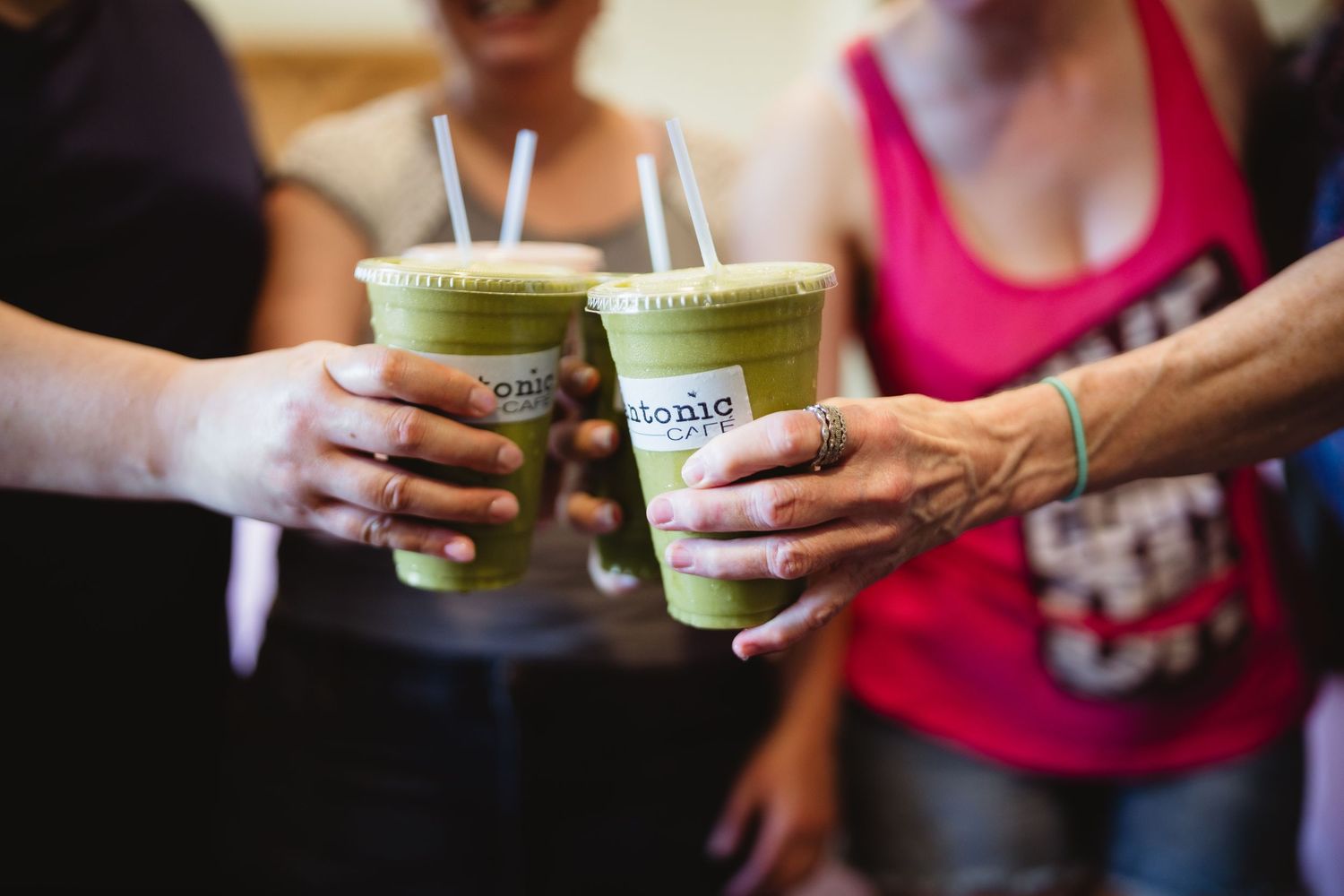 Two people holding green smoothie drinks in plastic cups with straws.