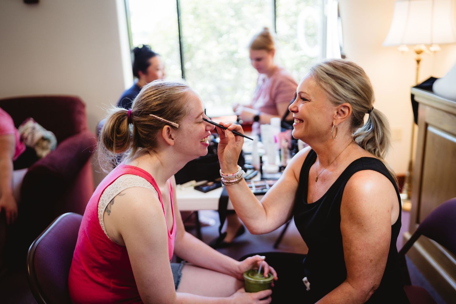 Wedding party members getting ready together in a room with natural lighting and joyful expressions.