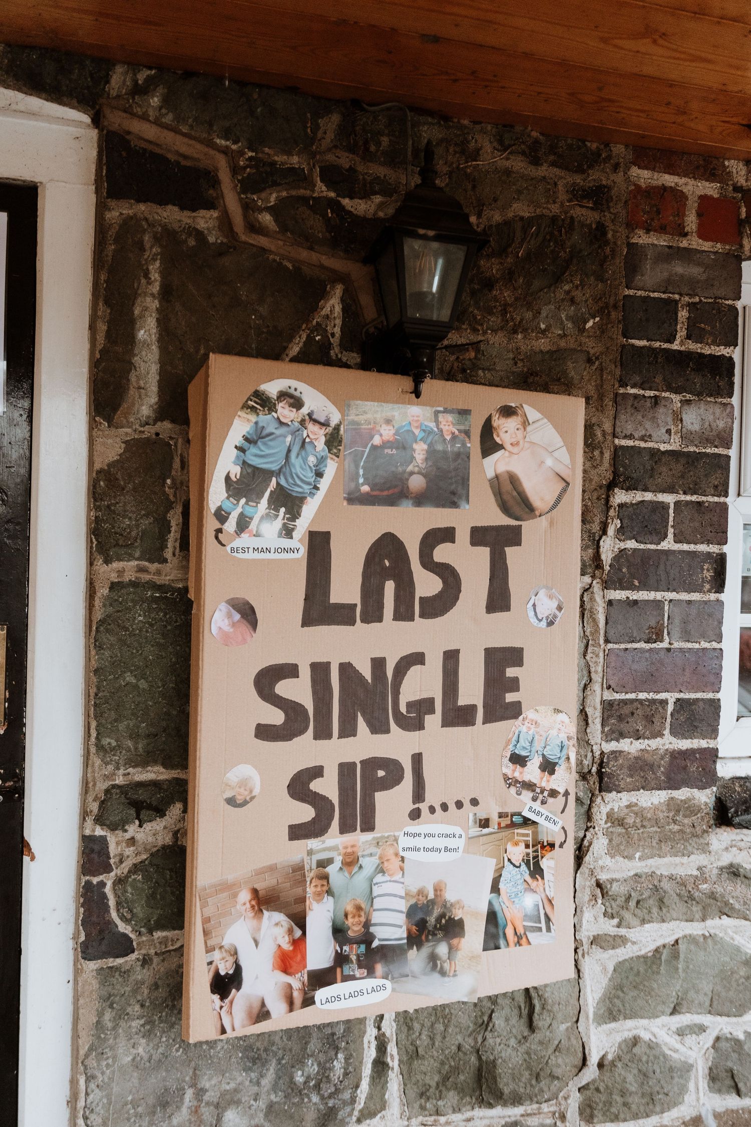A decorative photo board with 'Last Single Sip!' text and various photos pinned to it hangs on a stone wall under a lamp.