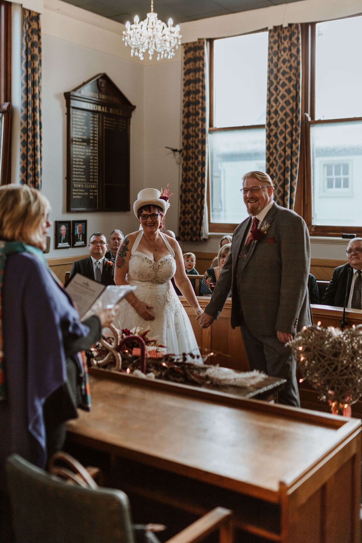 Small wedding ceremony in a classic wood-paneled room with chandeliers and pew seating.