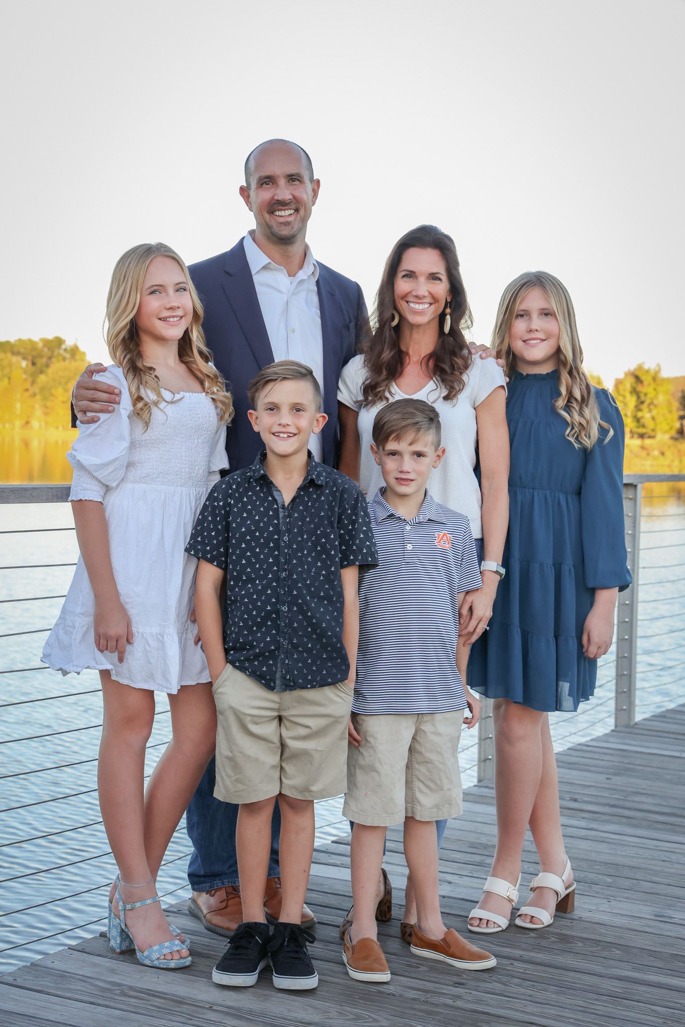 Family of six posing together on wooden dock with water and fall foliage behind them.