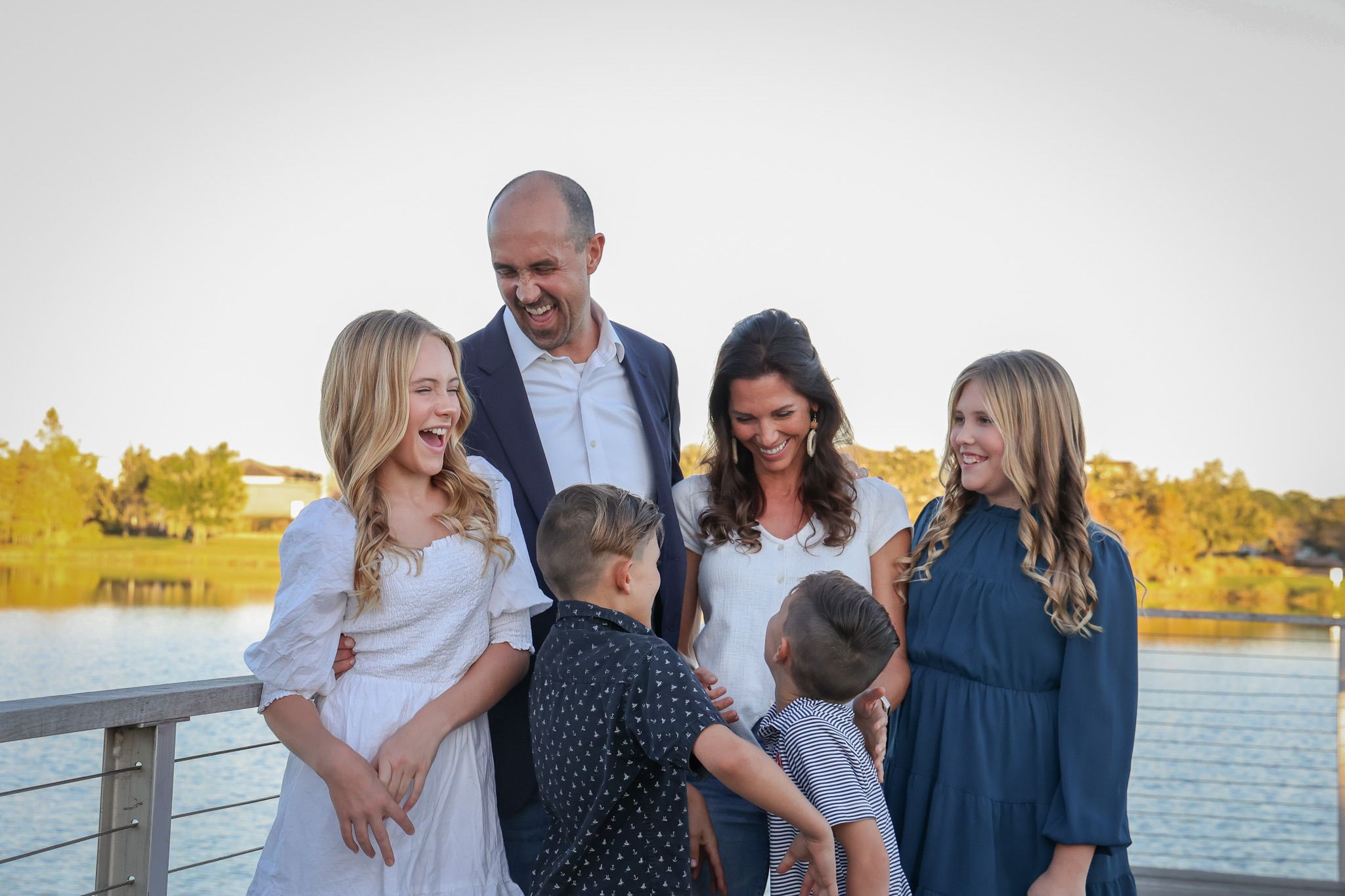 Family portrait on wooden dock with water and autumn trees in background.