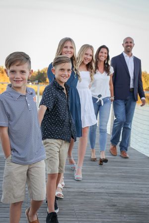 Casual family portrait on boardwalk with water and golden trees in background.