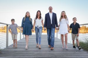 Family walking together on wooden boardwalk near water during golden hour.