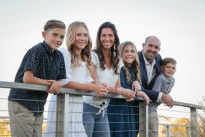 A family poses together on a wooden deck overlooking a scenic waterfront at sunset.