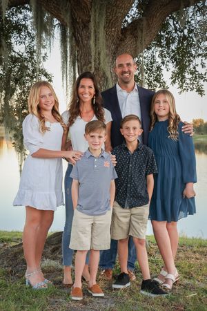 Family members in coordinated blue and white outfits pose together under a large oak tree.