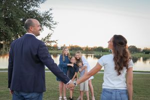 Family members interact and pose on grassy area near a lake during golden hour.