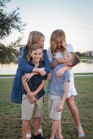 Candid moments of family members laughing and embracing on grass near water.