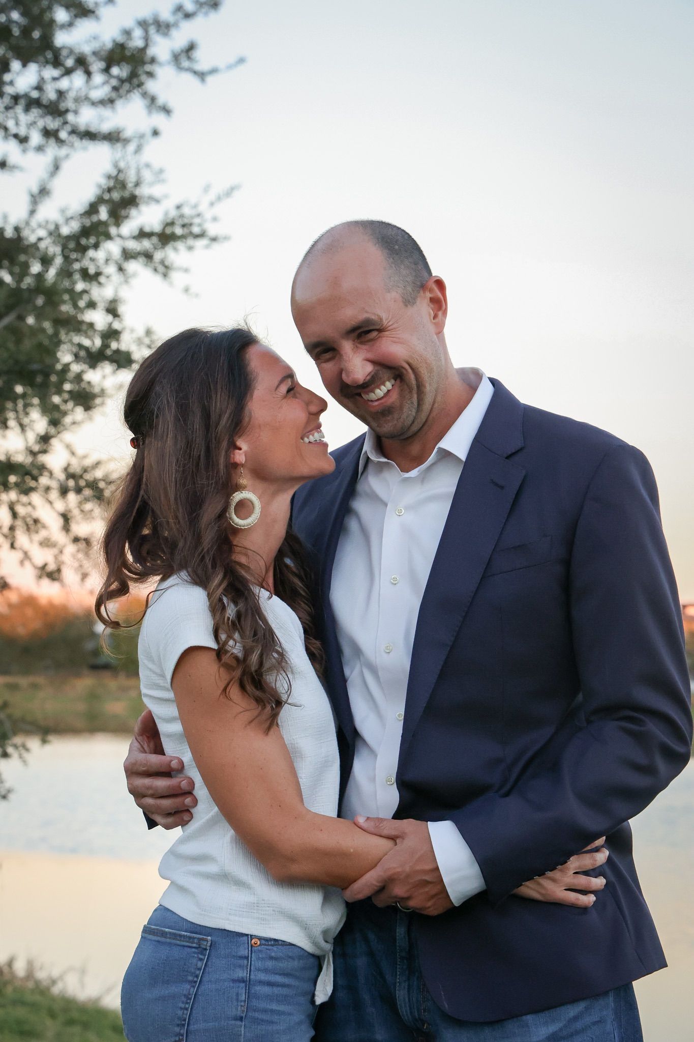 Couple shares intimate laughing moments together by waterfront at sunset.