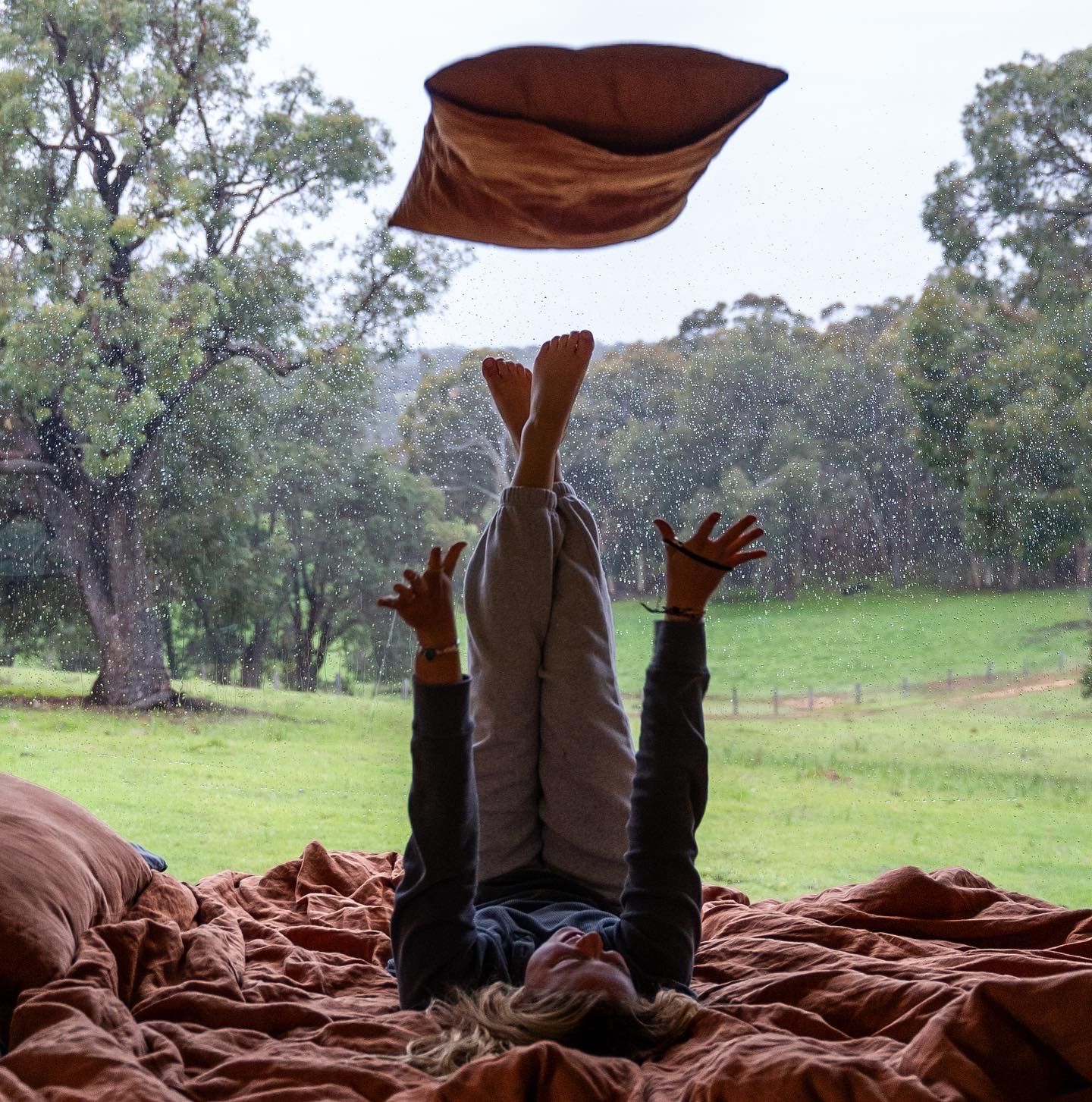 Playful moment captured throwing brown bedding in the air against a backdrop of green countryside and trees.