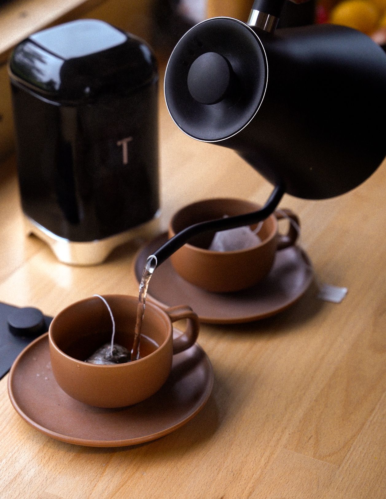 Coffee being poured into brown ceramic cups with modern black coffee maker on wooden surface.
