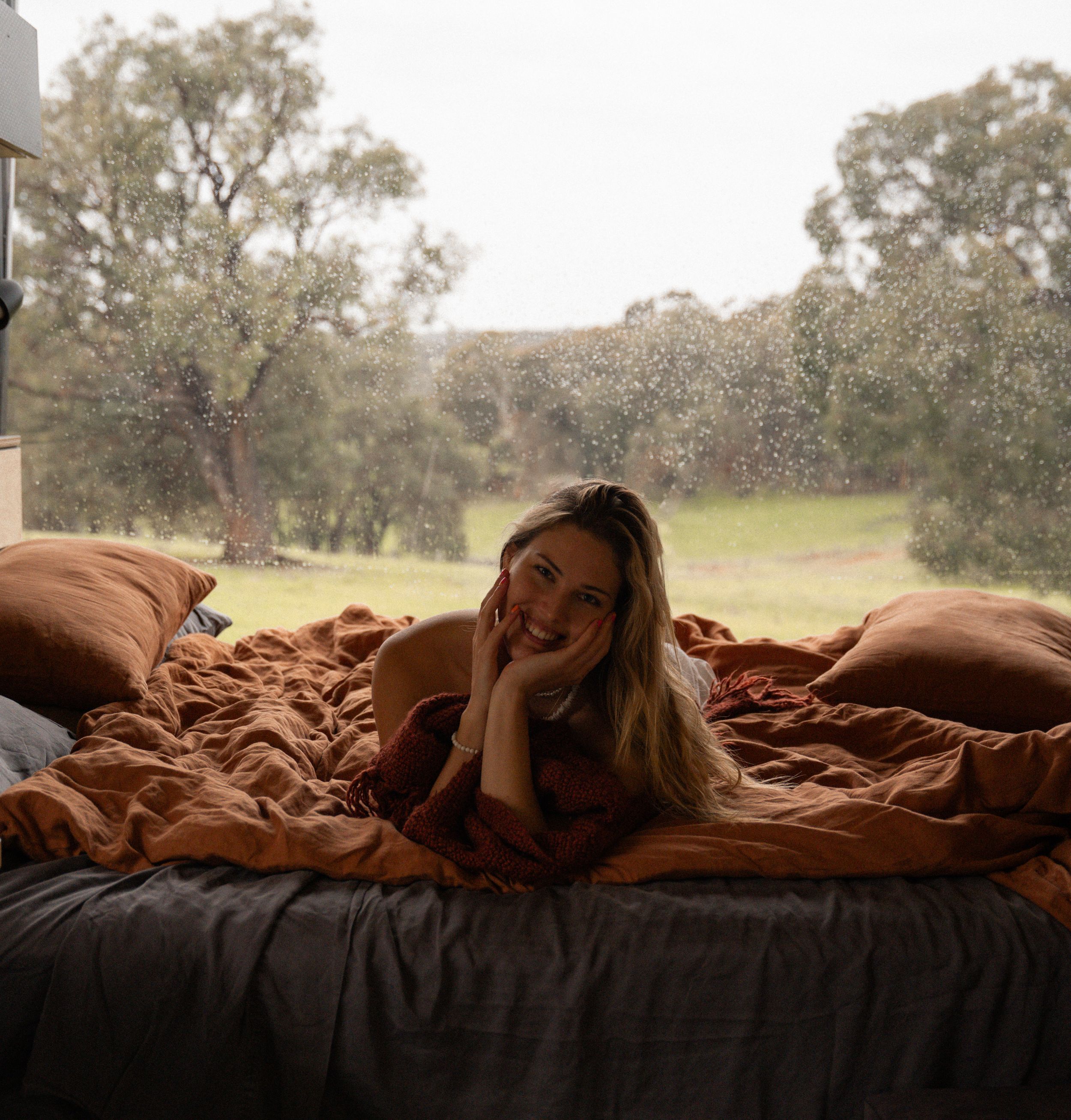 Relaxing moment in bed with rustic terra cotta linens overlooking scenic countryside.