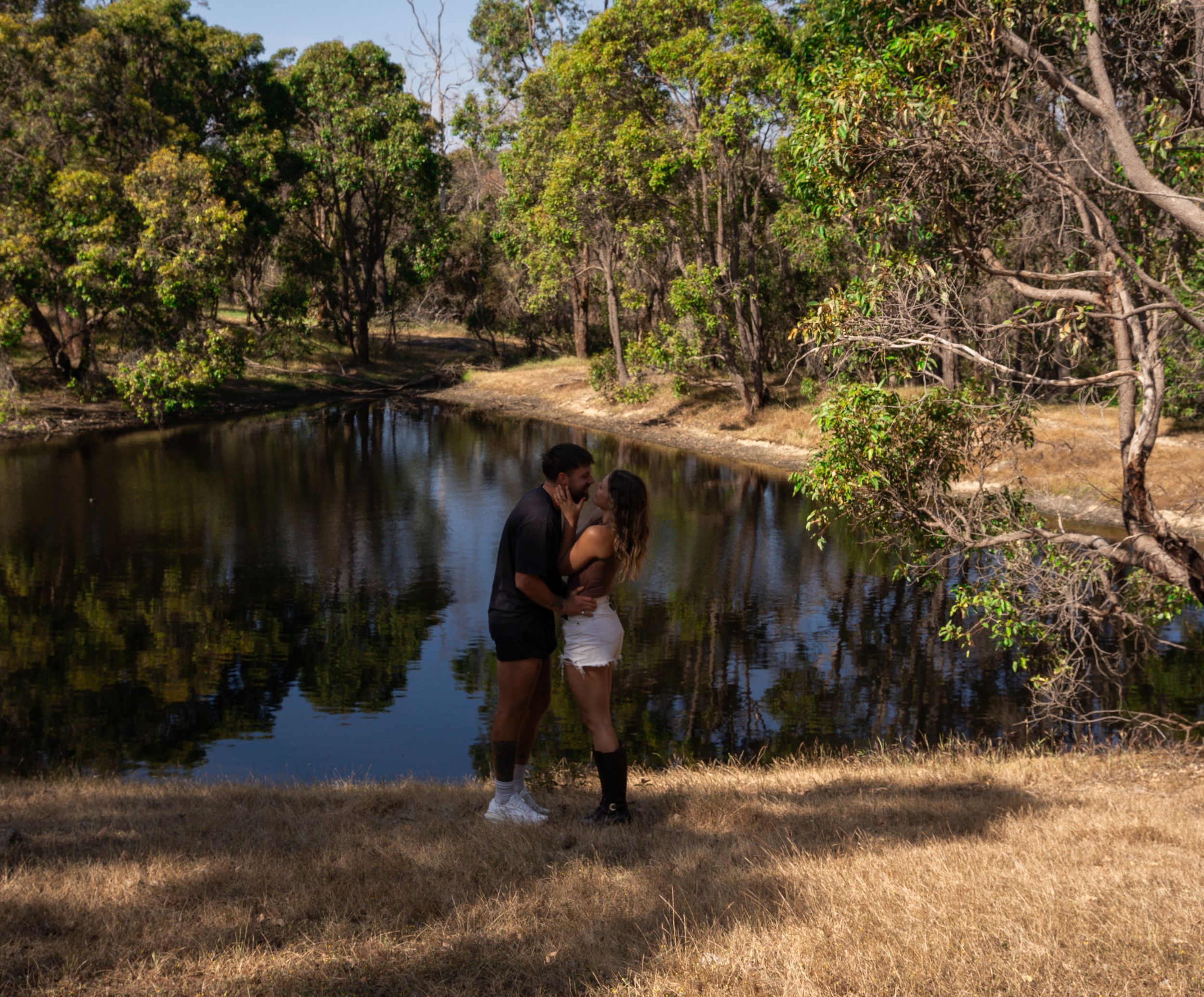 Romantic couple standing by tranquil pond surrounded by eucalyptus trees.