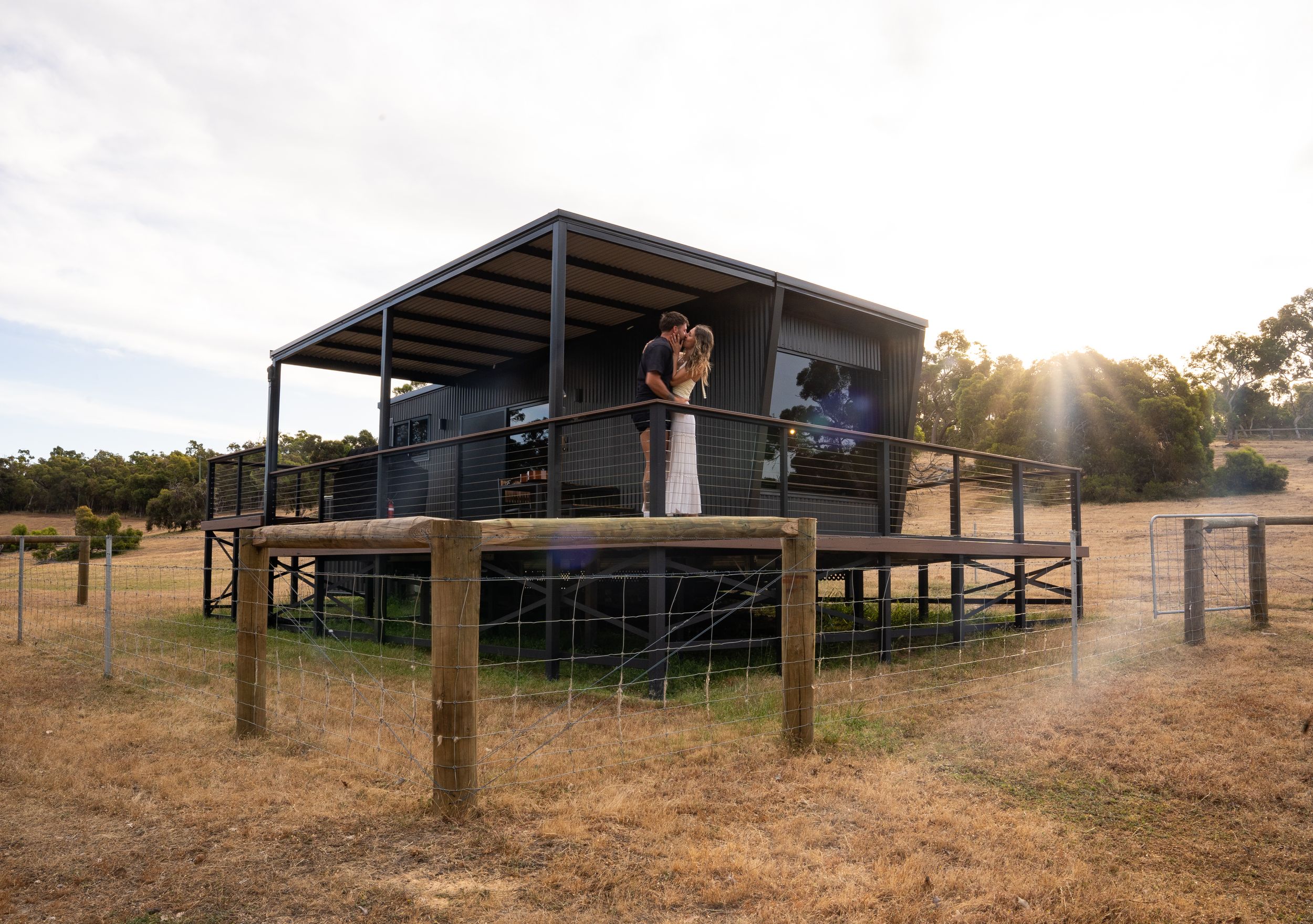 Modern elevated cabin structure with a deck in rural Australian bushland at sunset.
