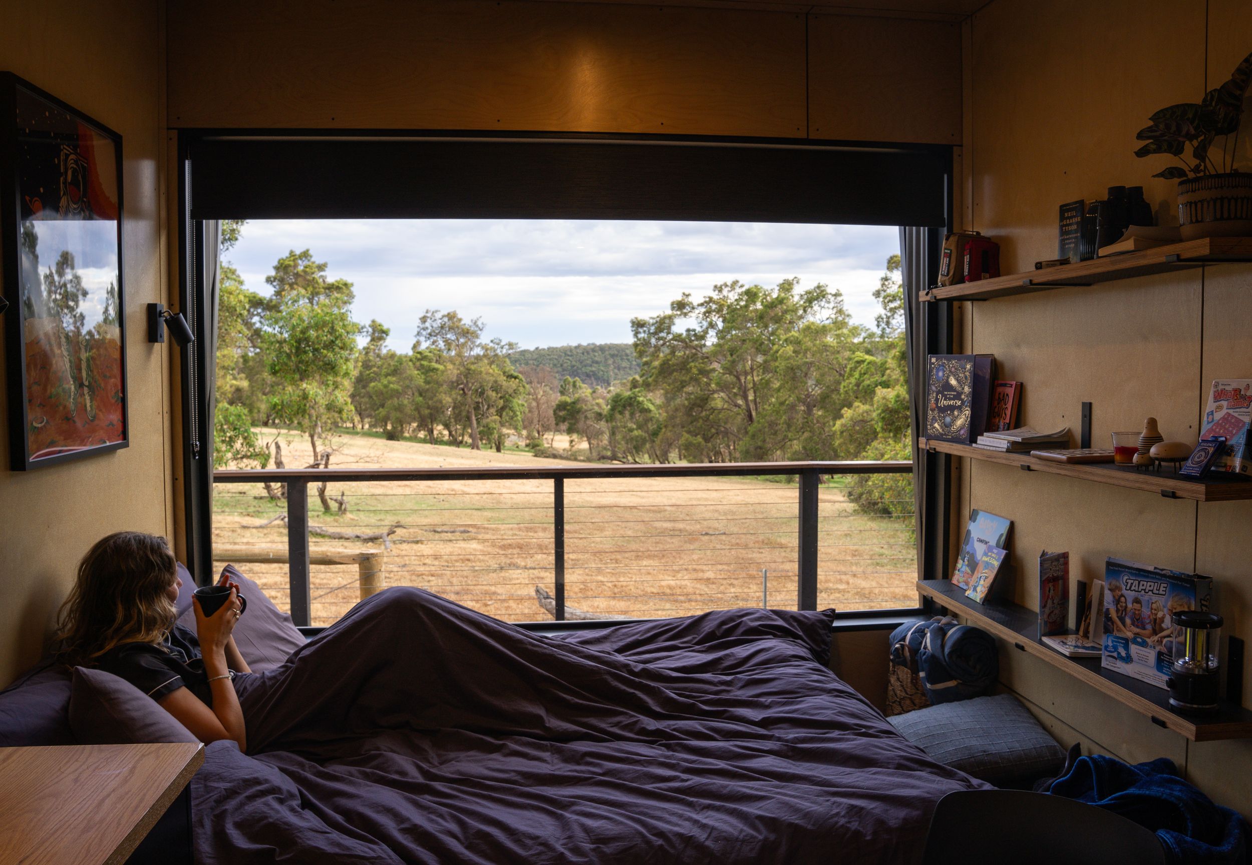 Cozy bed setup inside cabin with panoramic views of Australian bushland.