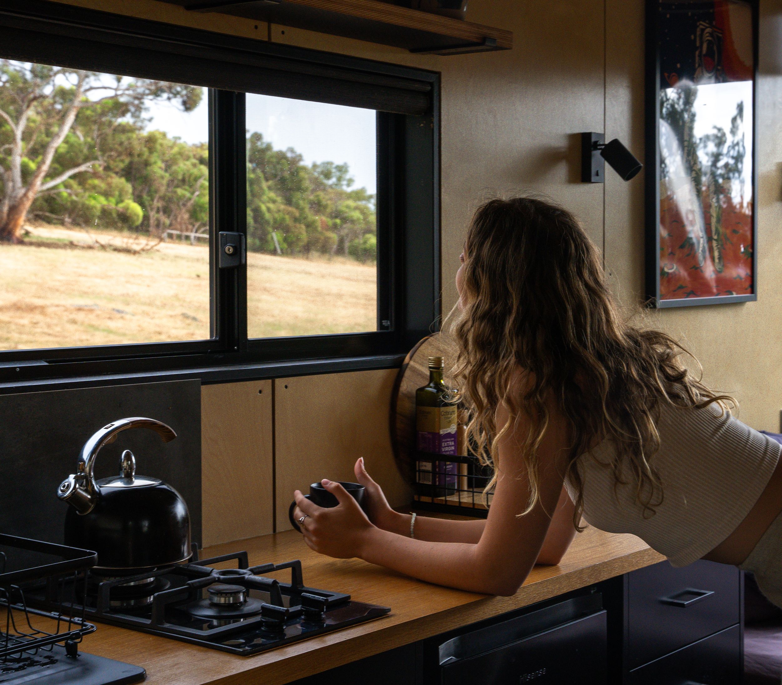 Looking out window while brewing coffee in compact camper kitchen.
