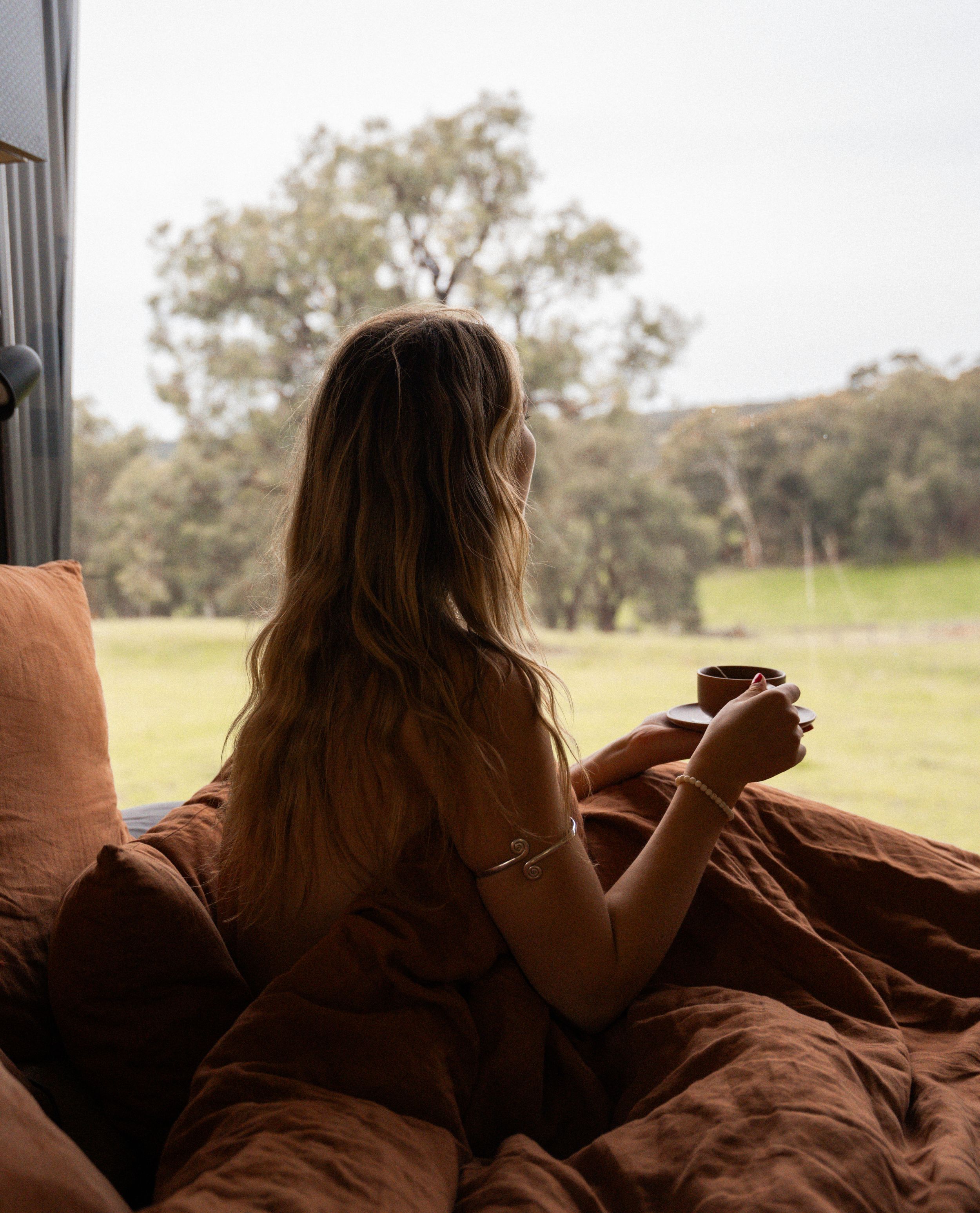Cozy morning scene overlooking Australian bushland with coffee cup and rustic bedding.
