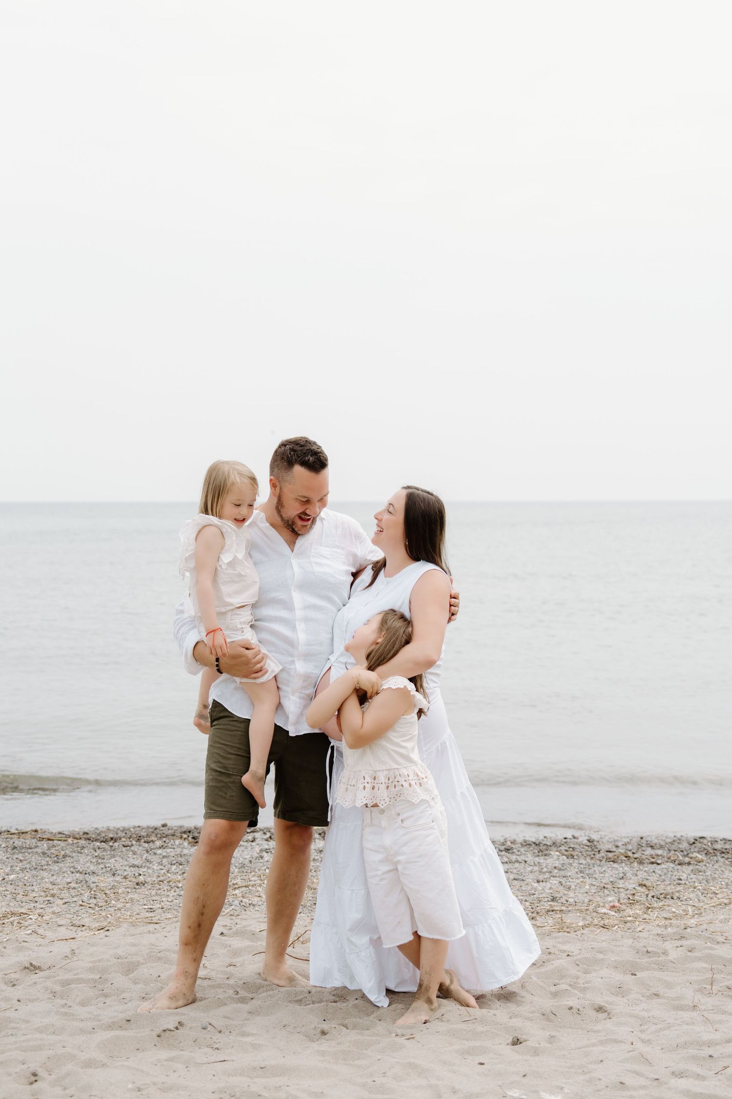 A family shares tender moments together on a beach with white sands and calm waters in the background.