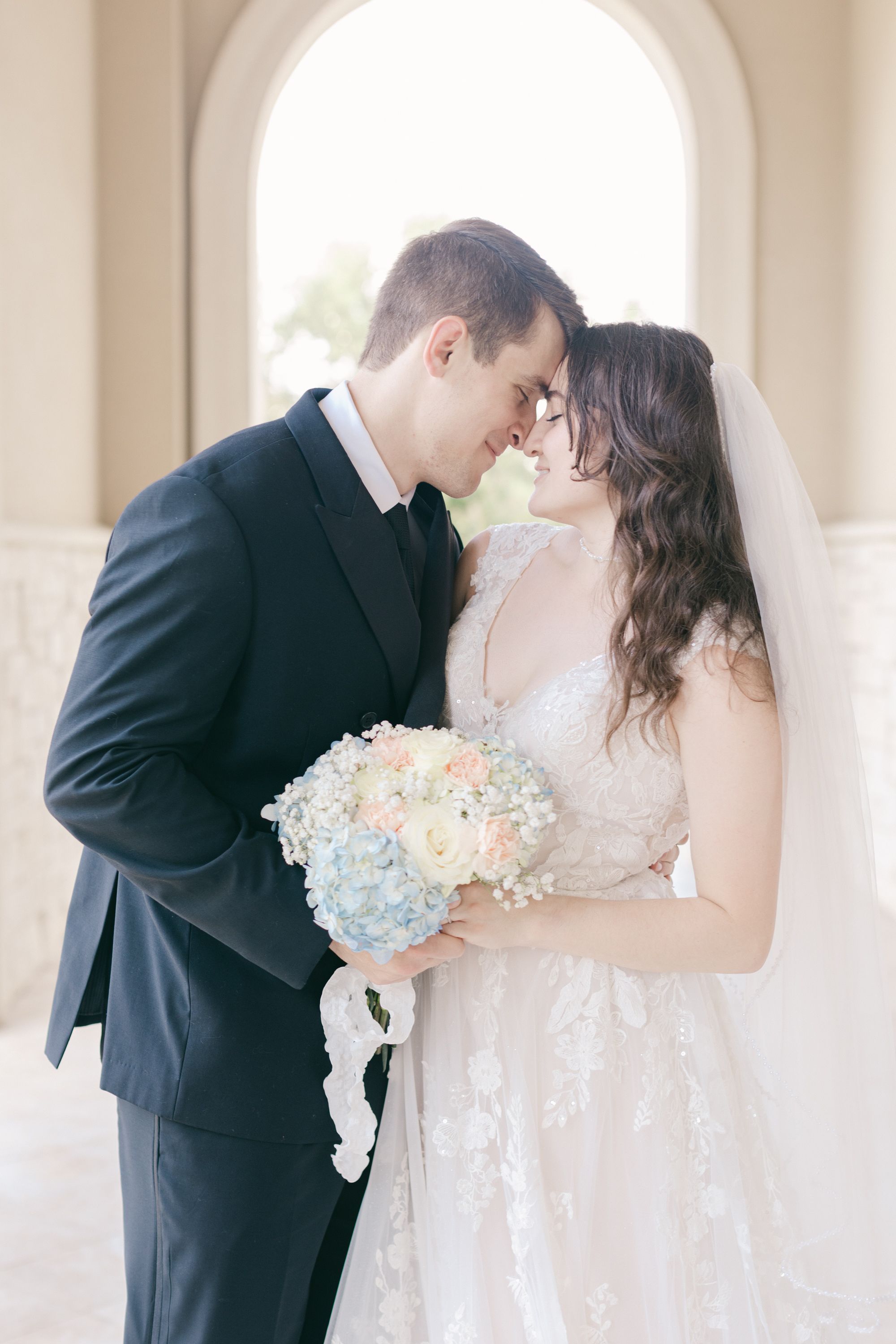 Romantic wedding portraits in an elegant white archway with soft natural lighting.
