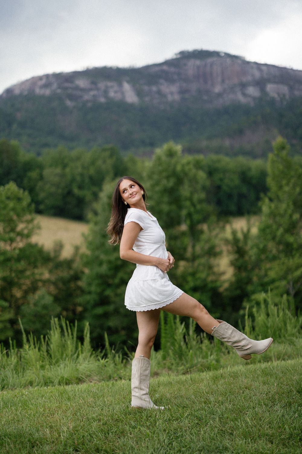 Someone in a white dress and knee-high boots poses in front of Table Rock Mountain in North Carolina.
