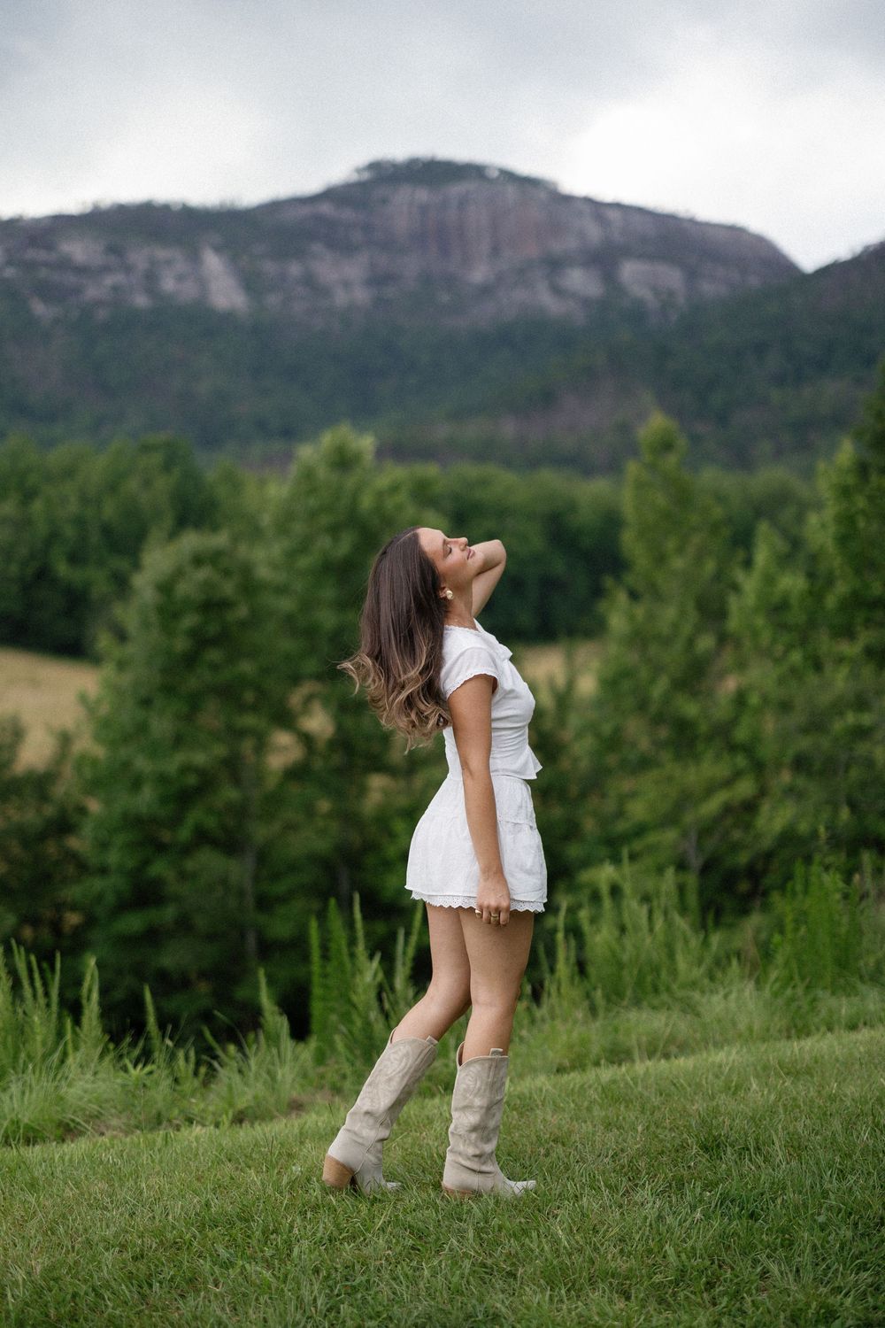 Someone walks through a grassy hill with mountains visible in the background on a summer day.