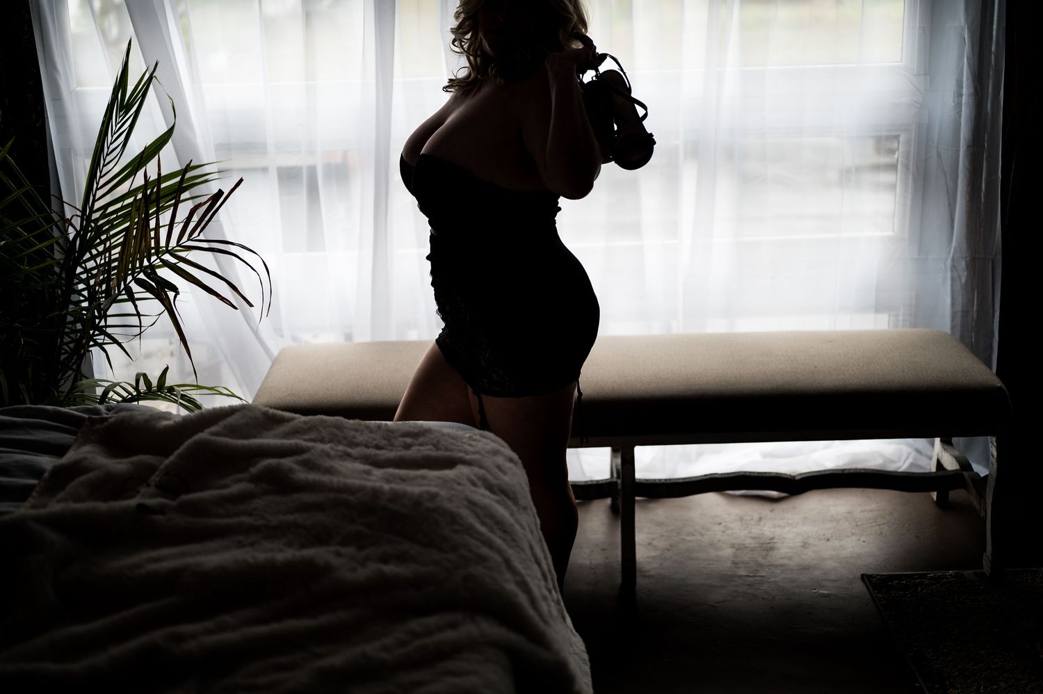 Silhouetted figure by window with potted plants creating moody atmosphere.