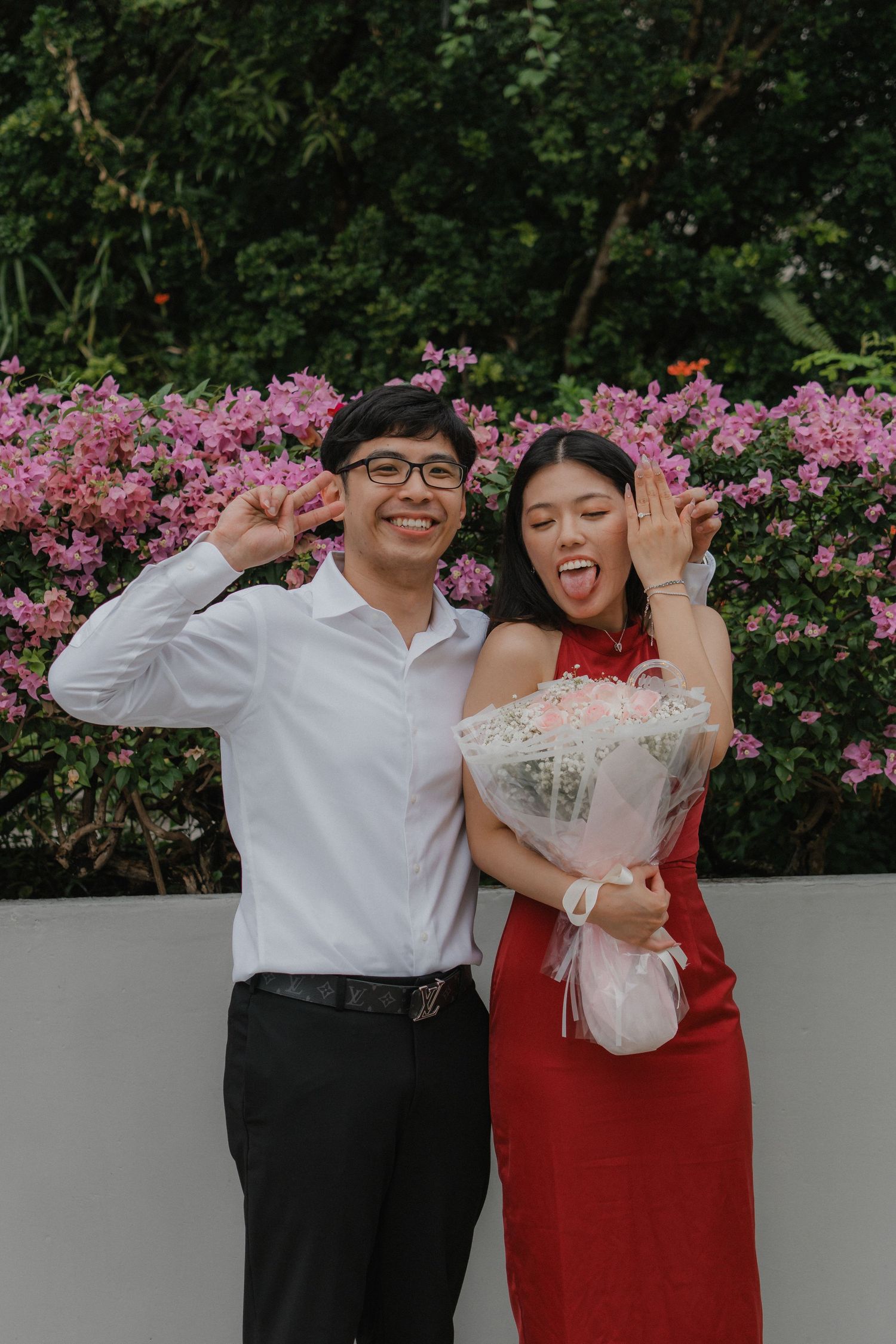 Joyful celebration moment in front of blooming pink flowers with a bouquet.