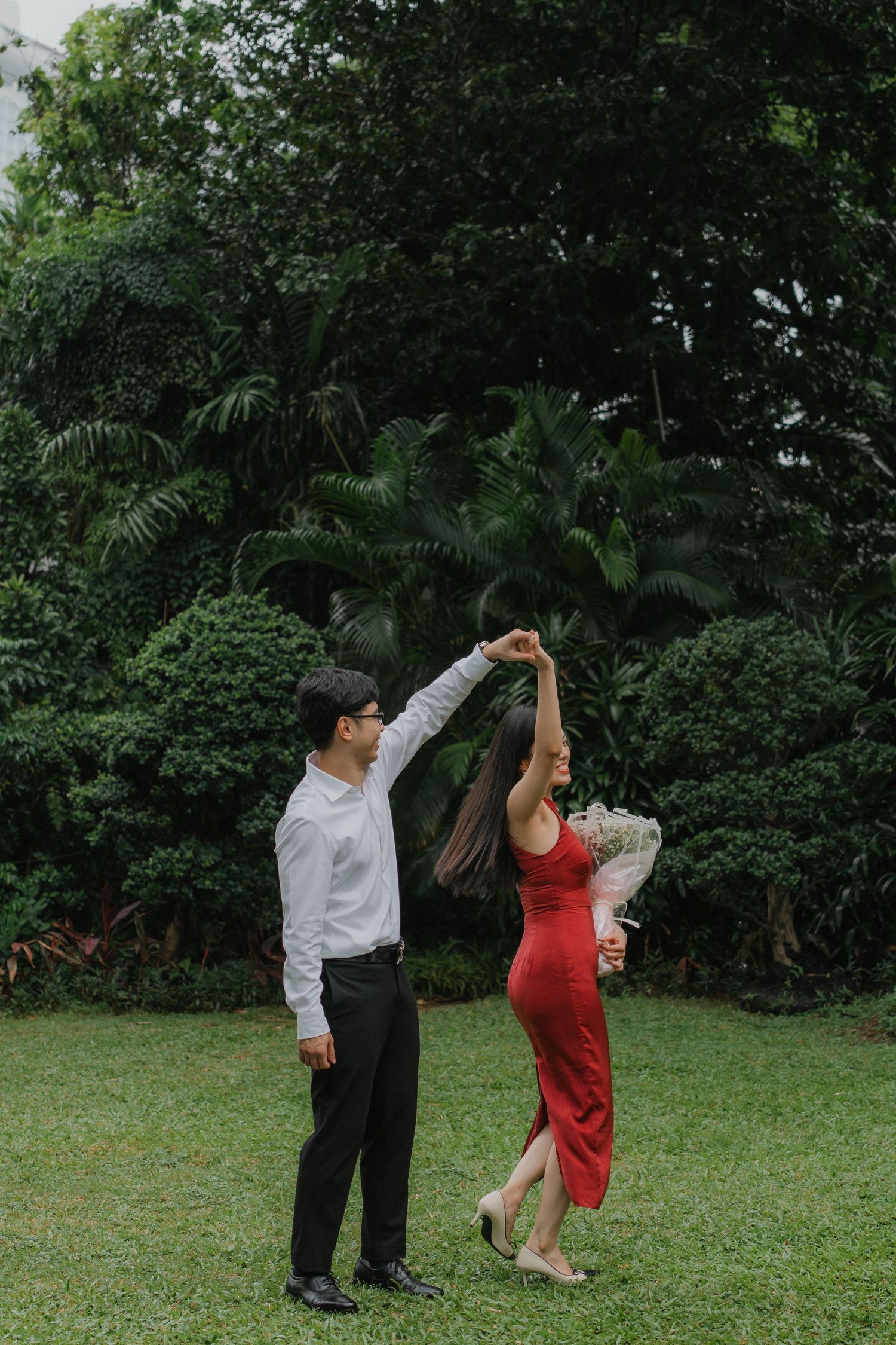 A couple dances together on a green lawn surrounded by lush tropical foliage in the background.