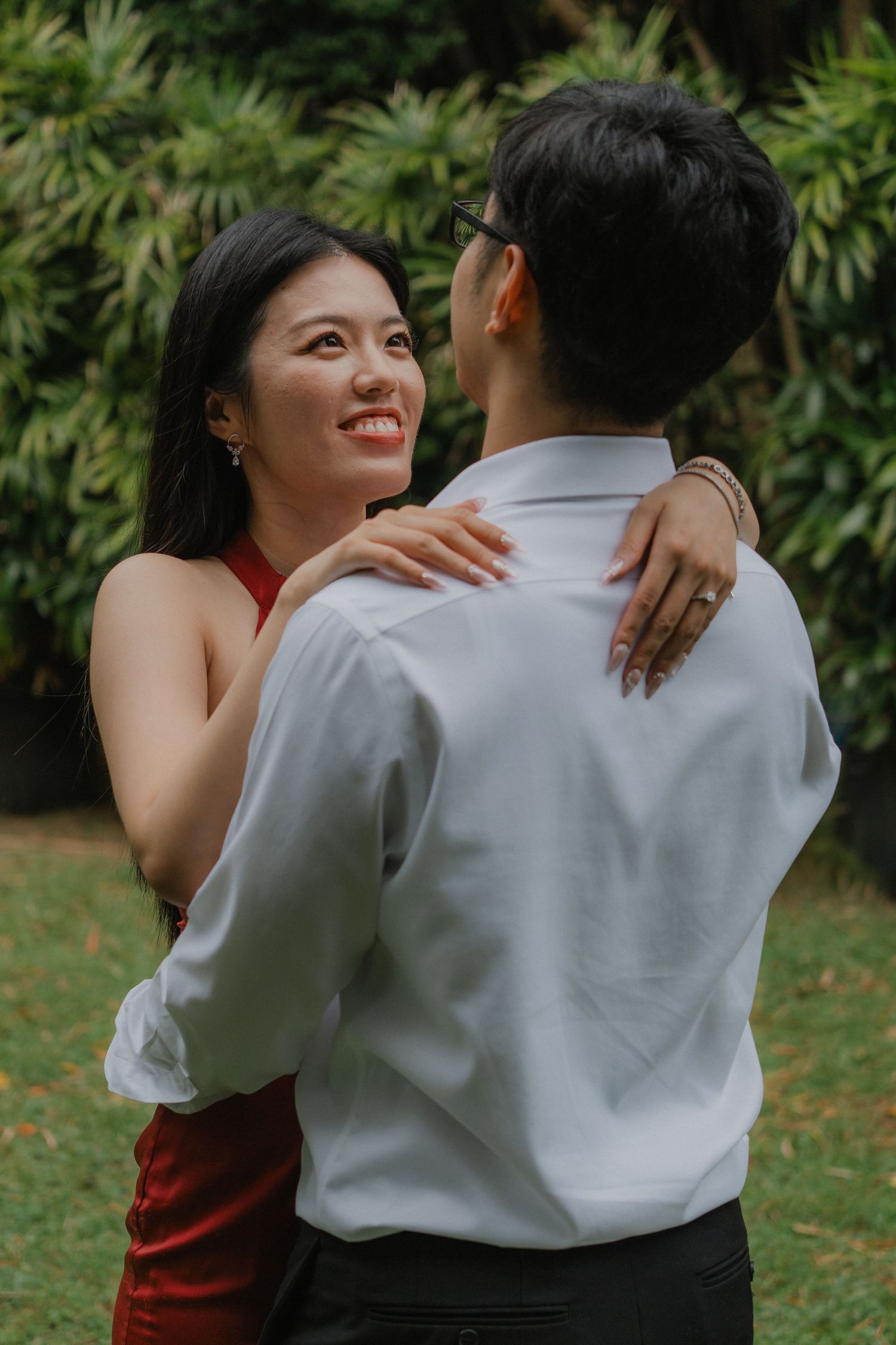 A romantic couple embraces outdoors in a garden setting, with lush green foliage in the background.
