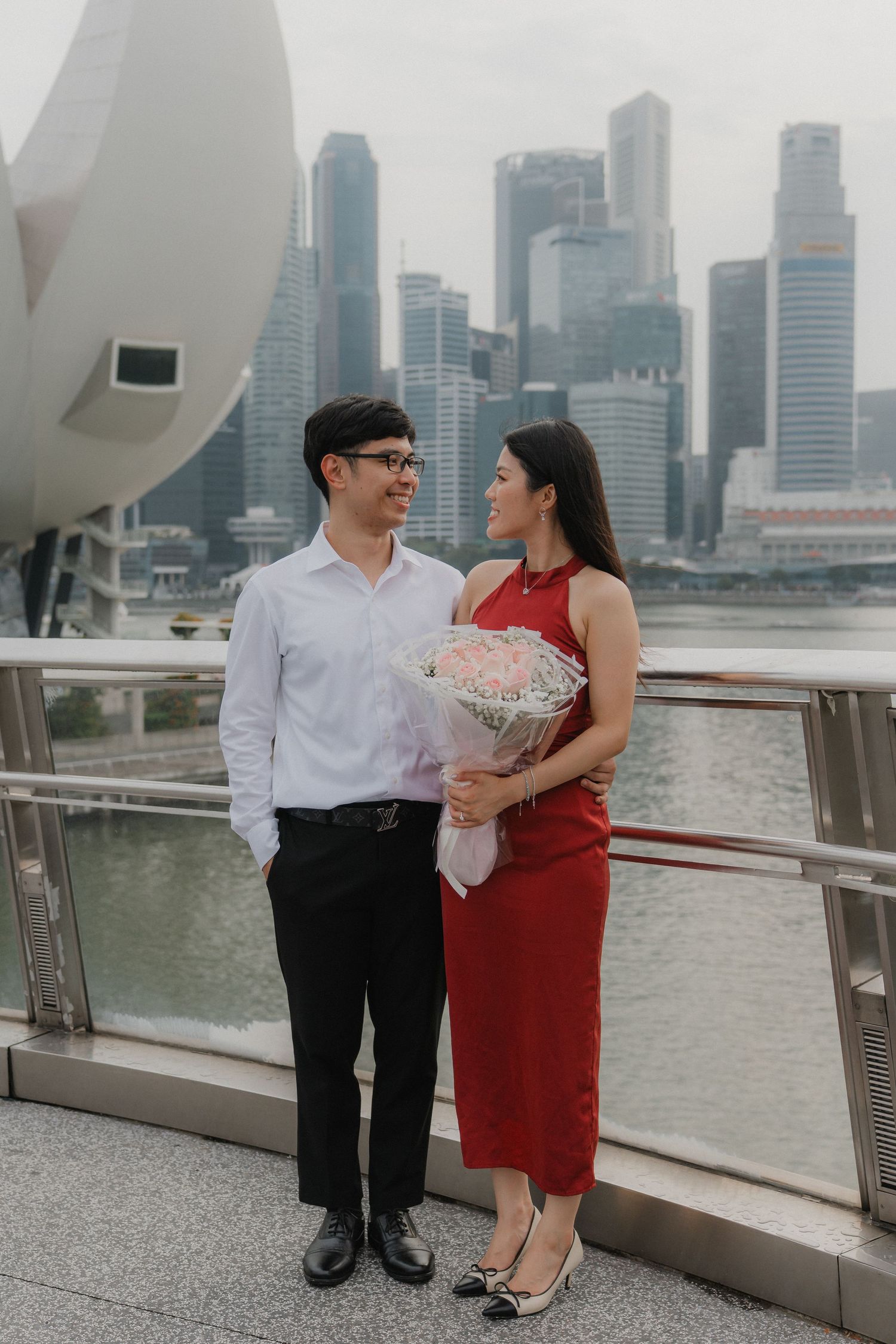 A couple poses with a bouquet against Singapore's downtown skyline along Marina Bay waterfront.