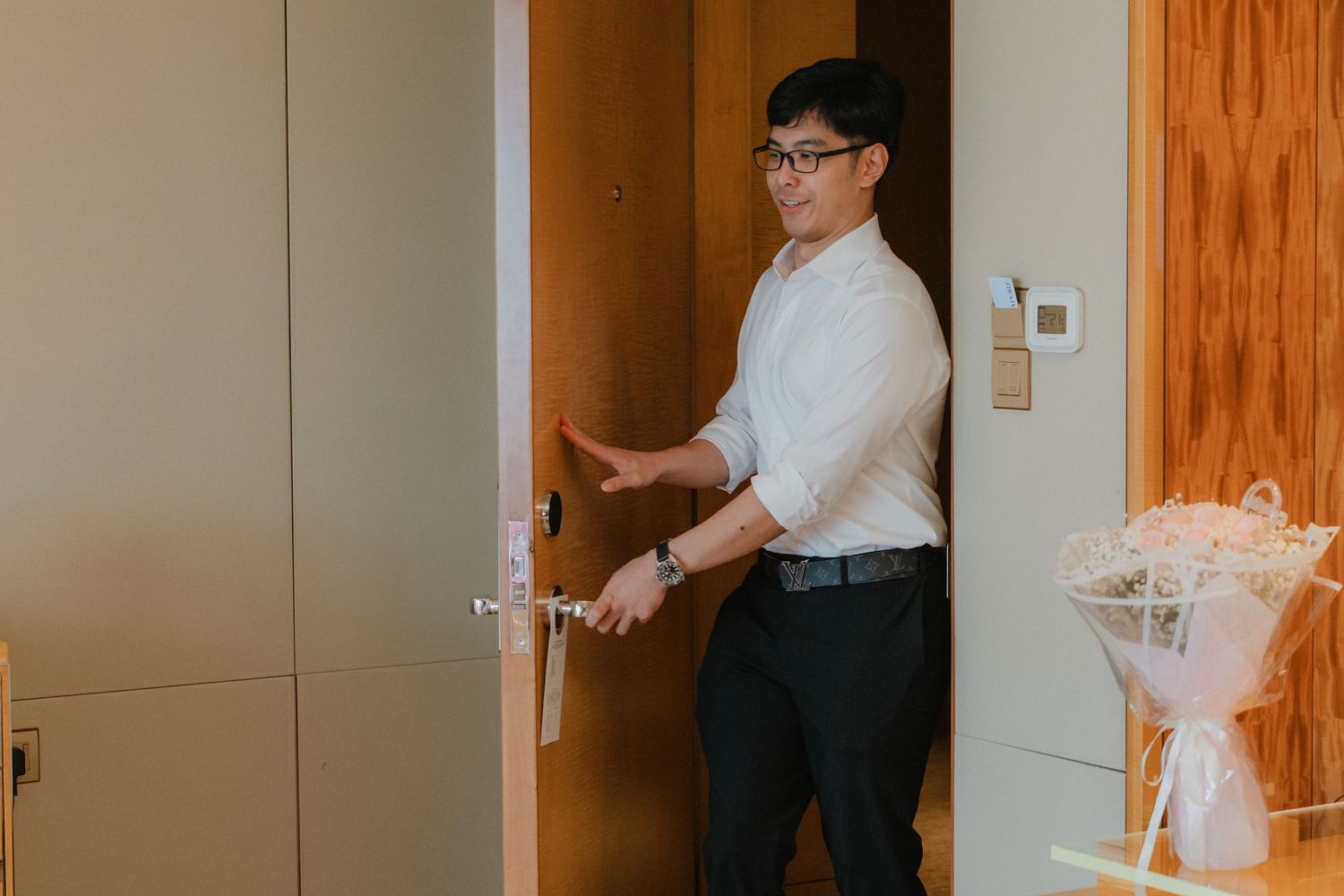 Hotel staff member in white uniform carries folded clean white towels down a wooden-paneled hallway.