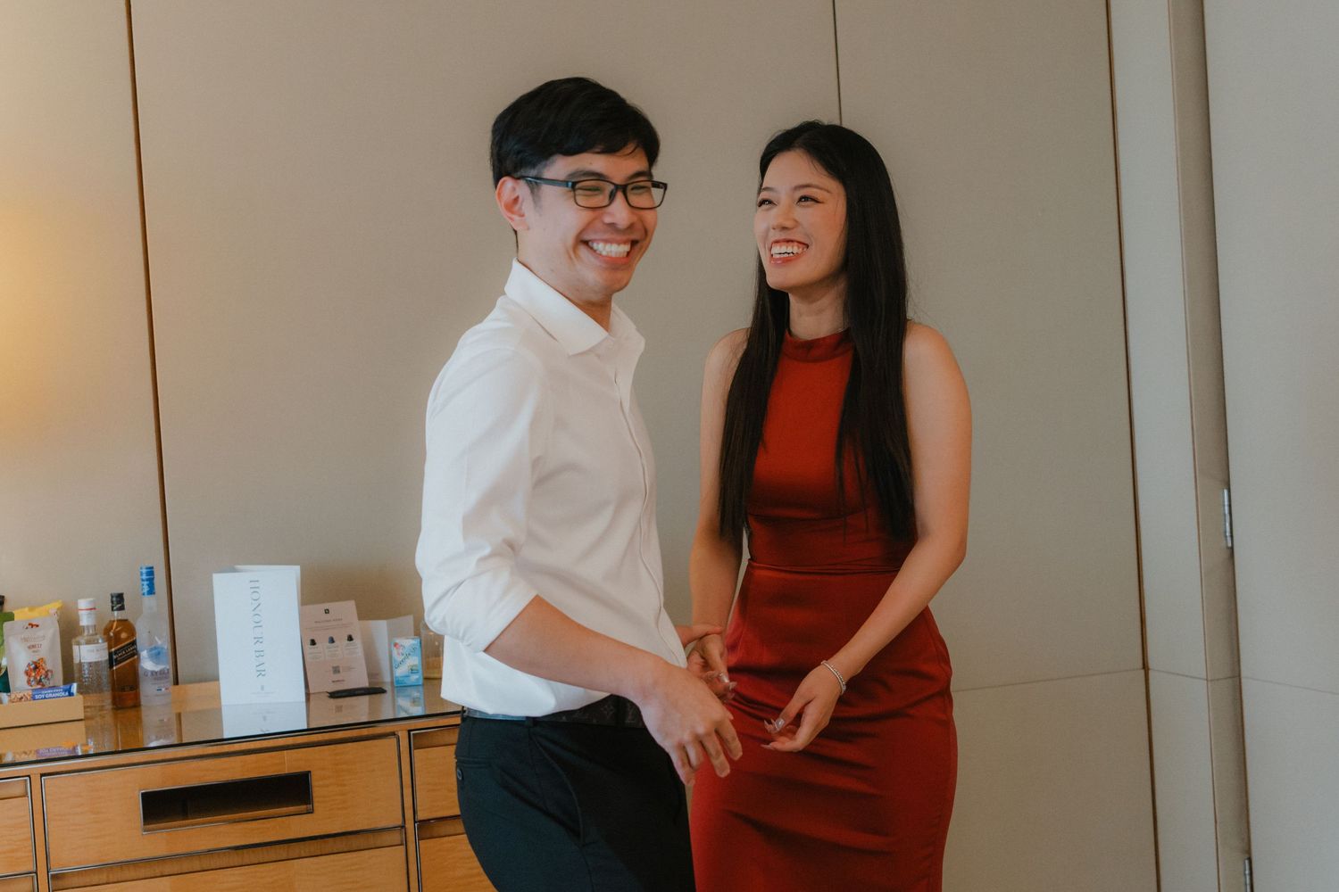 A couple shares a joyful moment together in their home, with the woman wearing a red dress and the man in white.