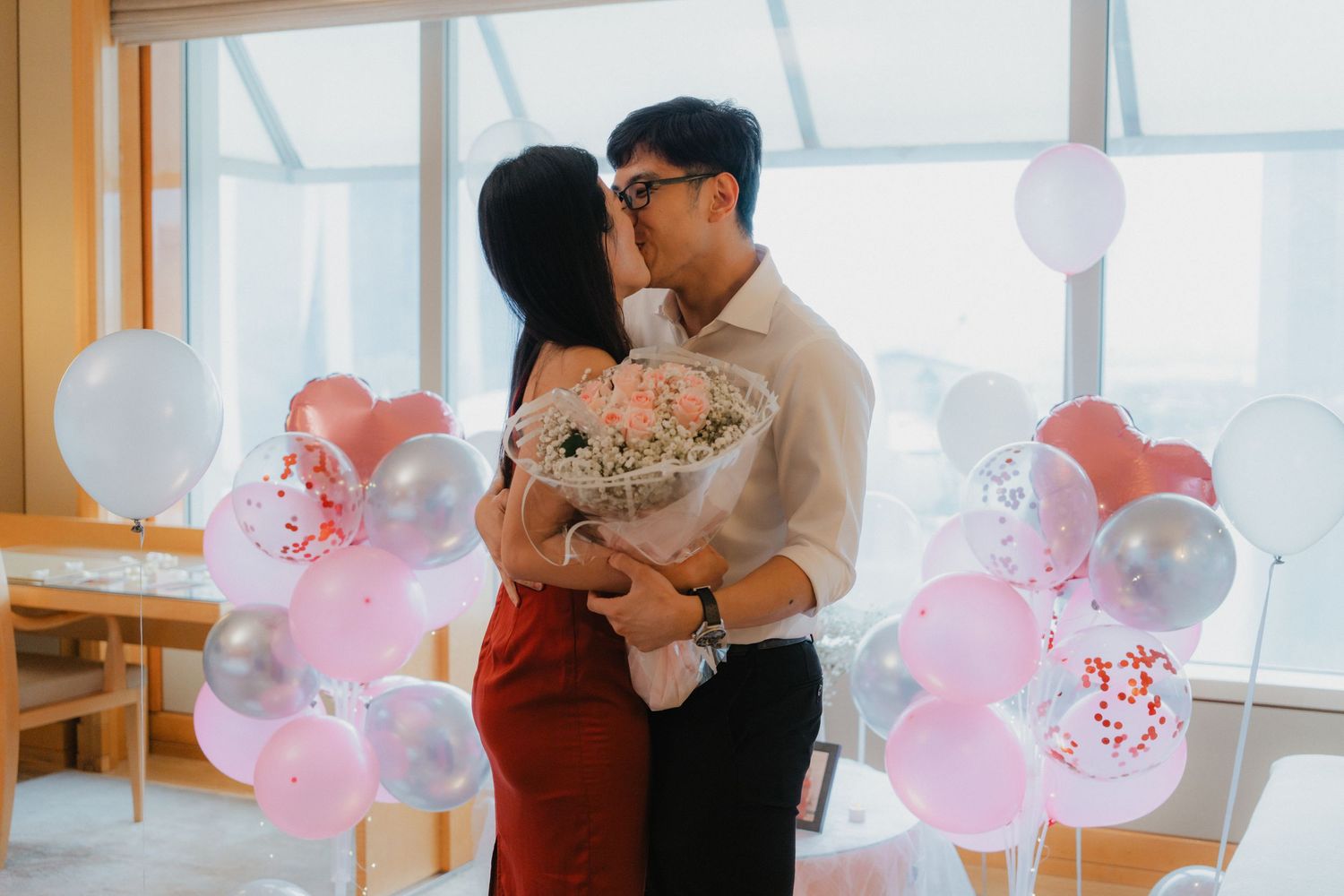 A couple sharing an emotional proposal moment surrounded by romantic balloon decorations.